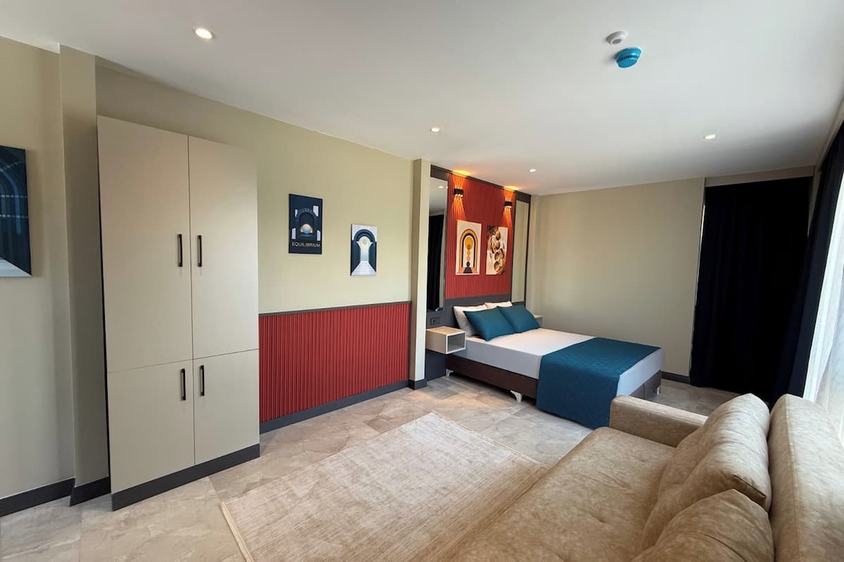A modern hotel room with a bed, a sofa, a wardrobe, and a red accent wall.