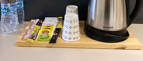 A table with a stainless steel kettle, two water bottles, a mug, and some snacks.