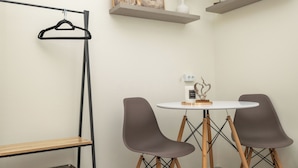 A modern room with a round table, two chairs, a hanging garment rack, and decorative items on shelves. - Nobia 5 (Athens)