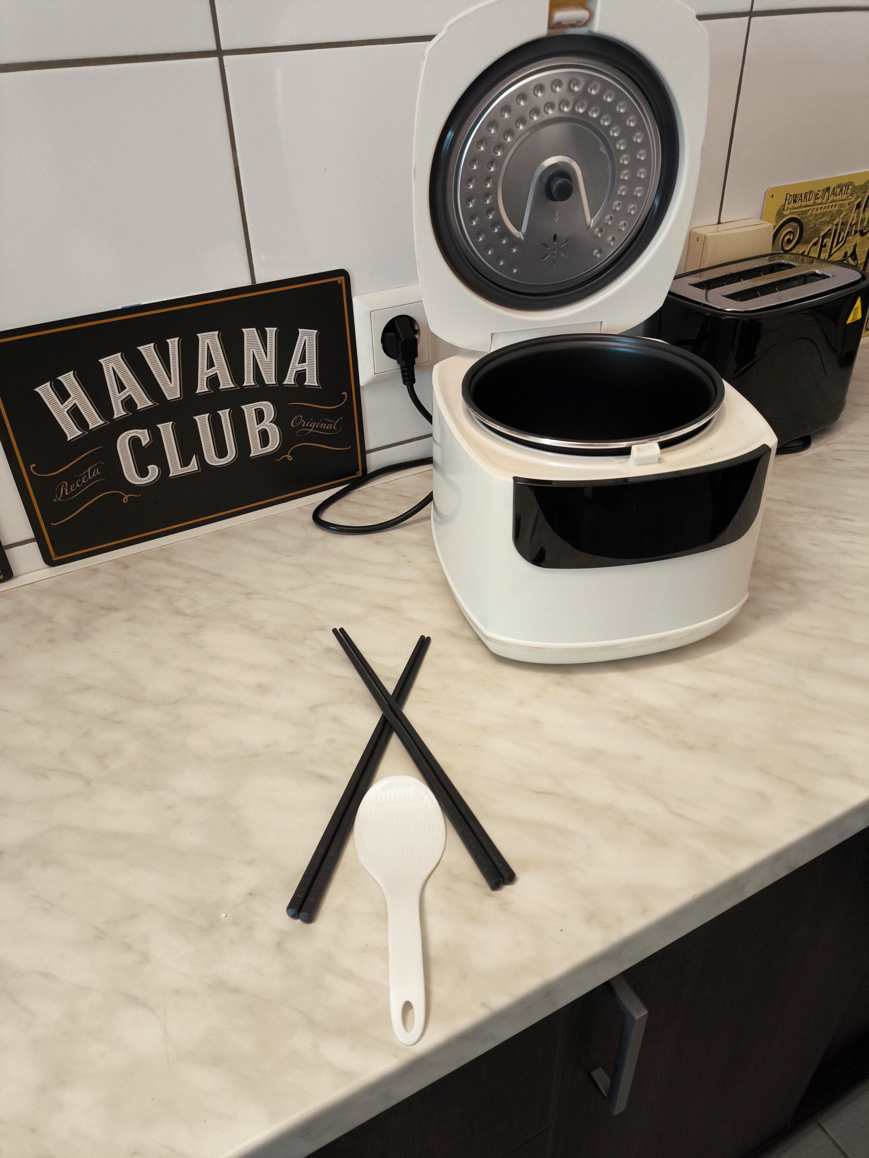 A kitchen counter with a rice cooker, chopsticks, and a sign that reads "HAVANA CLUB Original."