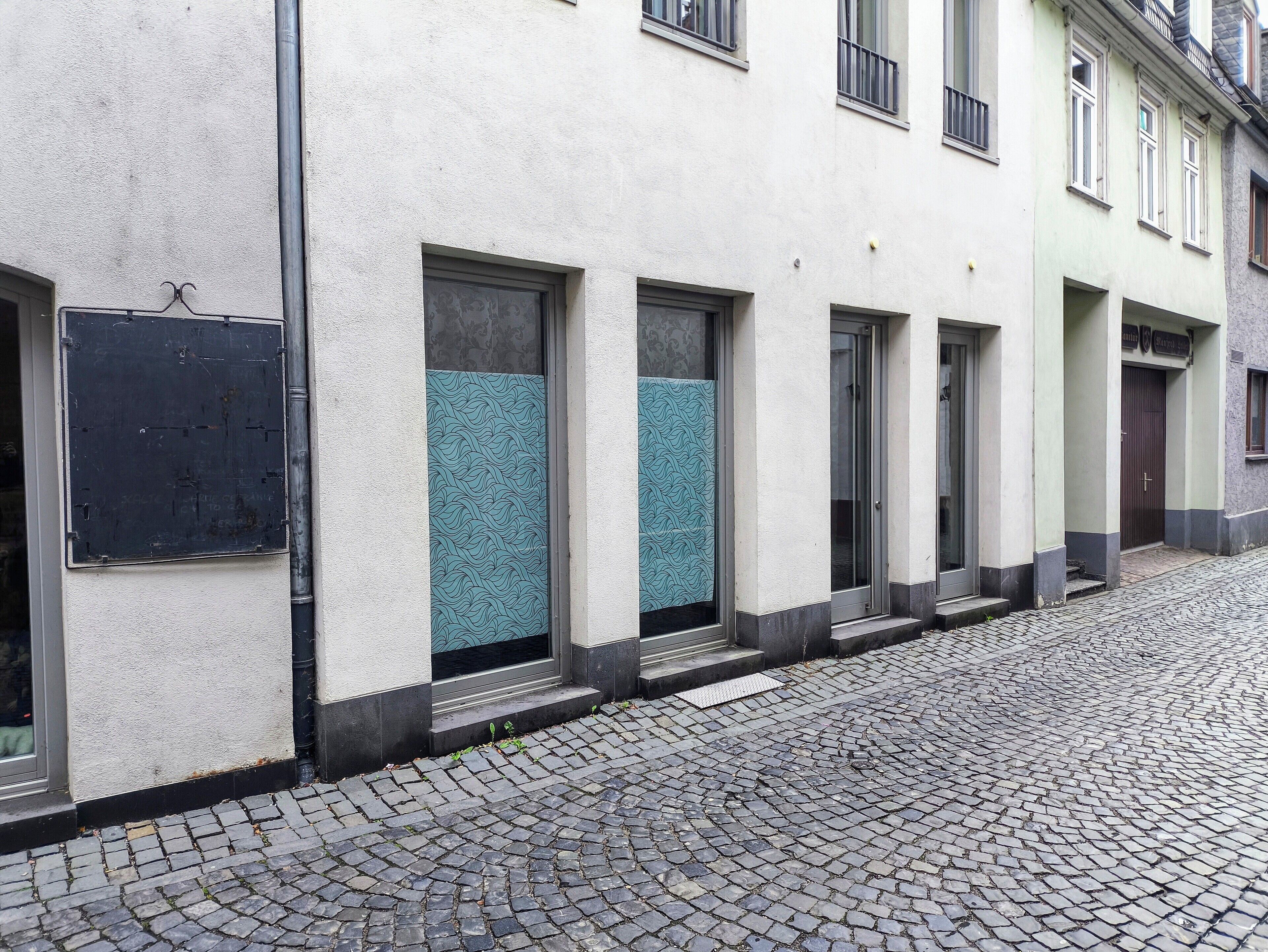 Una hilera de edificios con ventanas y puertas grandes, algunos con rejas de metal, en una calle empedrada.