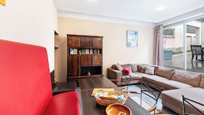 Ein modernes Wohnzimmer mit einem roten Sofa, einem Holzschrank, einem braunen Sofa und einem Esstisch mit Korb und Holztasse.