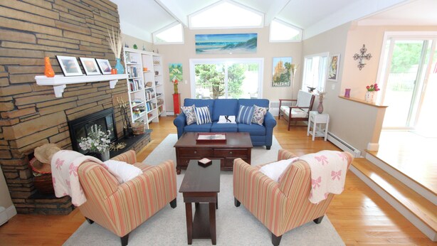 A living room with a fireplace, a blue sofa, striped armchairs, a coffee table, and a bookshelf.