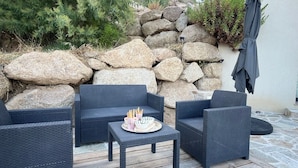 A patio with wicker furniture, a small table with food, and a stone wall backdrop. - Large 50m2 studio, in the heart of the Maquis, San gavino di Figari (San gavinu Di figari)