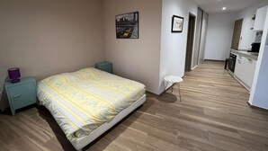 A bedroom with a bed, a small bedside table, a nightstand, a wall-mounted picture, and a hallway leading to a kitchenette. - Large 50m2 studio, in the heart of the Maquis, San gavino di Figari (San gavinu Di figari)
