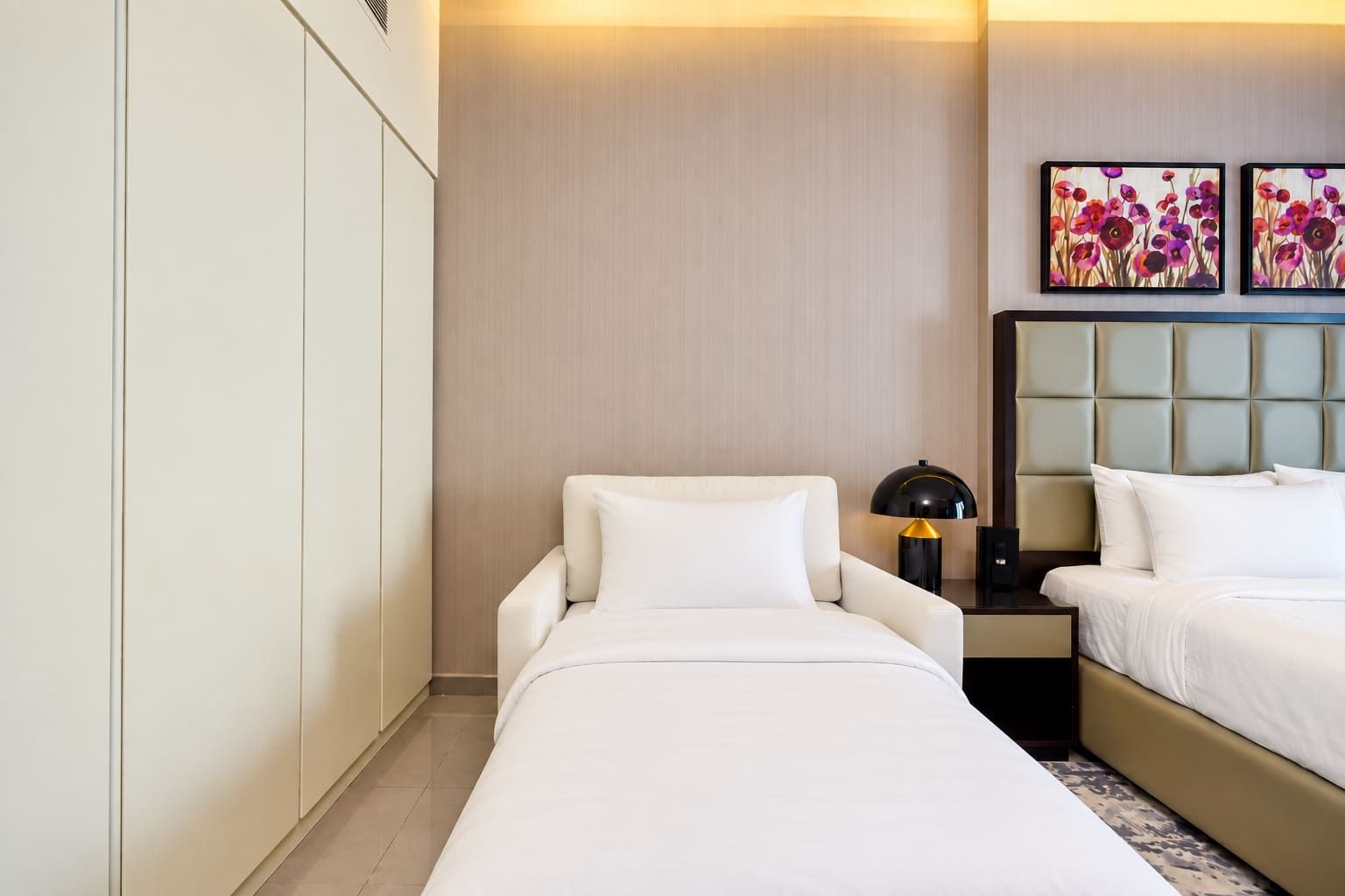 A hotel room with two beds, a nightstand, a lamp, and artwork on the wall.