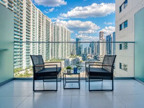 Un balcone con due sedie e un tavolino, affaccia su una città con grattacieli.