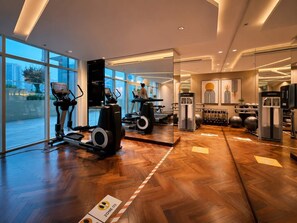 A modern gym with exercise equipment, large windows, and a herringbone floor pattern.