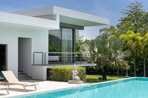 Een modern huis met een zwembad, een standbeeld en weelderige begroeiing.
