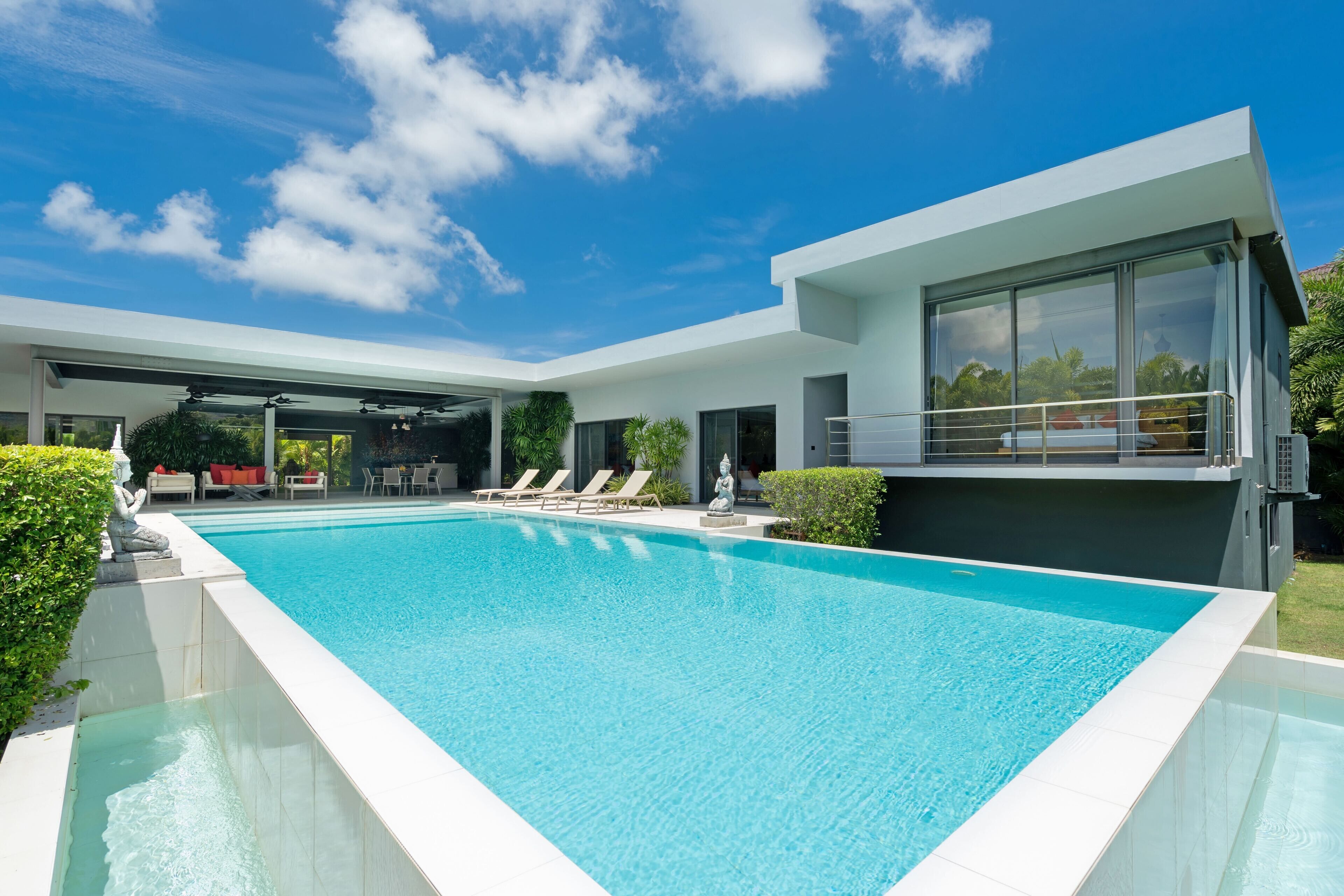 Ein modernes Haus mit Swimmingpool, Sitzgelegenheit im Freien und großem Fenster mit Blick auf den Pool.