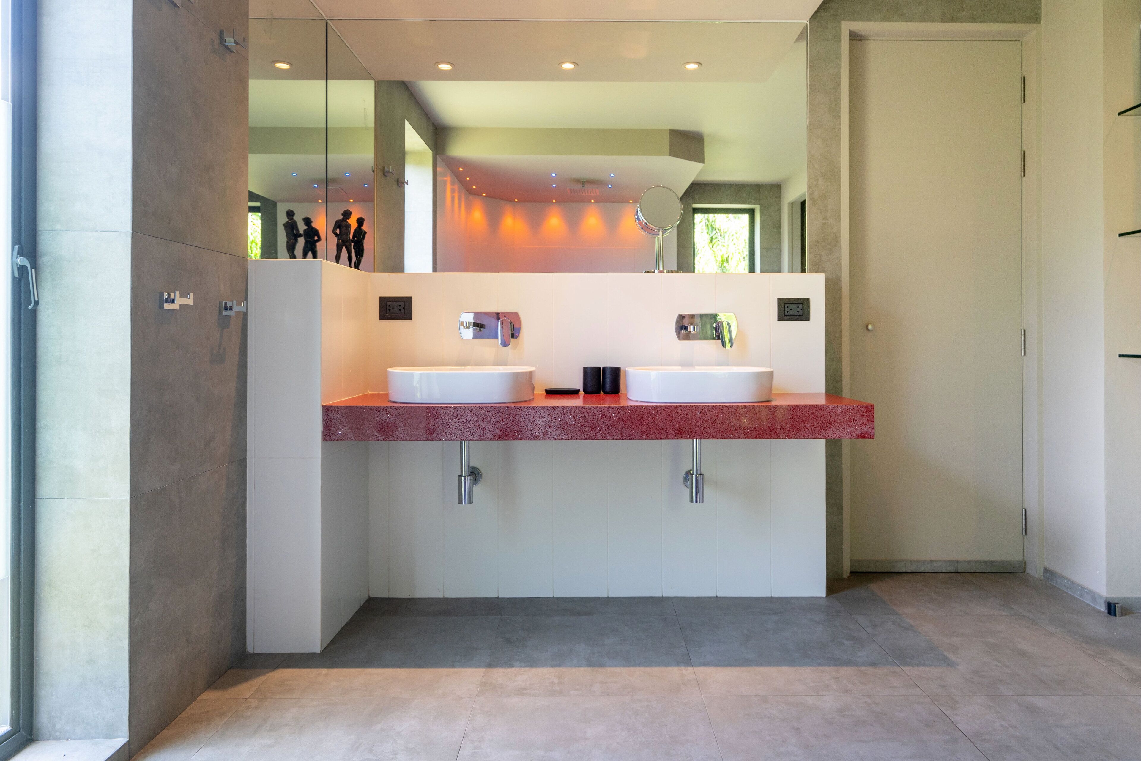 A modern bathroom with two sinks, a large mirror, and a red countertop.