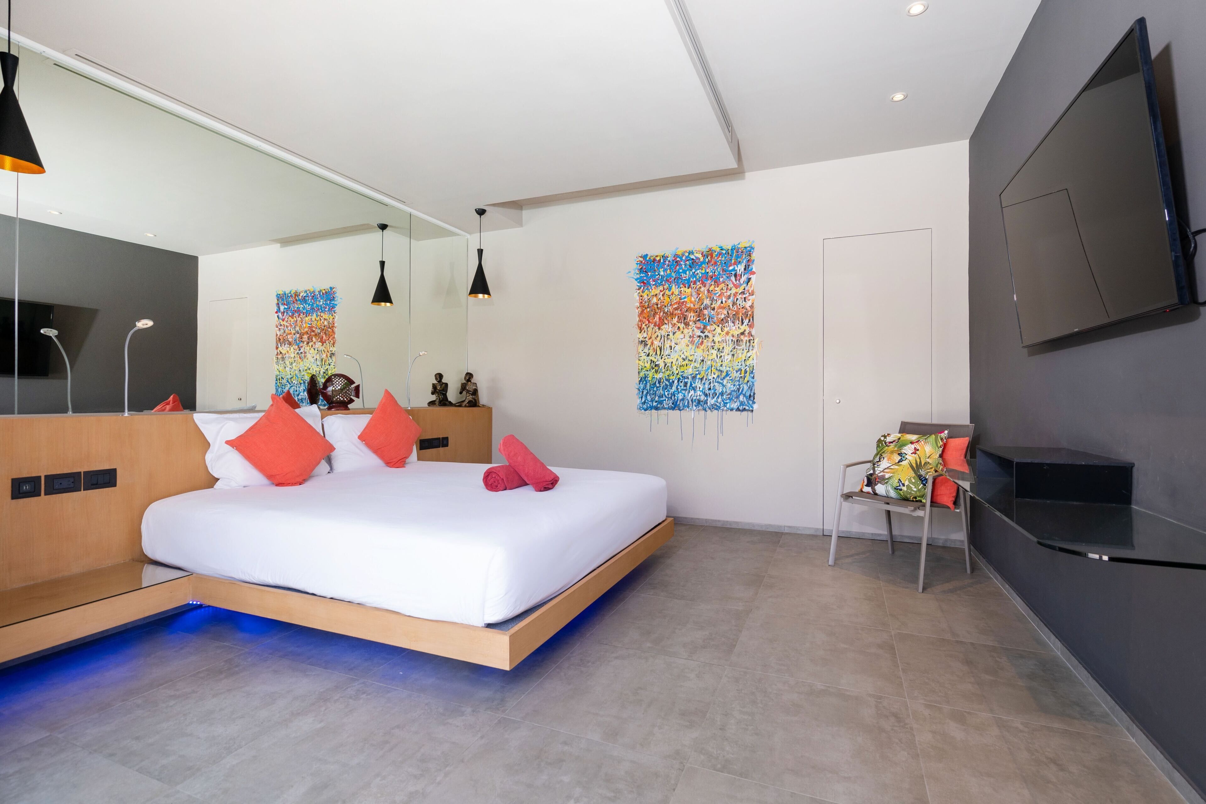 Een moderne slaapkamer met een bed, een televisie, een stoel en kunstwerken aan de wanden.