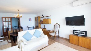 A living room with a sofa, TV, wooden cabinet, and a dining area with a table and chairs. - EUROMAR - 3 bedroom apartm - Cullera - wifi (Cullera)