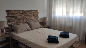 A bedroom with a stone headboard, a bed with beige linens, two folded blue towels, and a nightstand with a lamp. - 3 bedroom apartment in val d'arcomie (Val d'Arcomie)