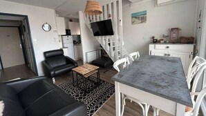 A modern living room with a black leather sofa, a small wooden coffee table, and a dining table with white chairs. There is a staircase with a TV mounted on the wall above it. - 3 bedroom apartment in val d'arcomie (Val d'Arcomie)