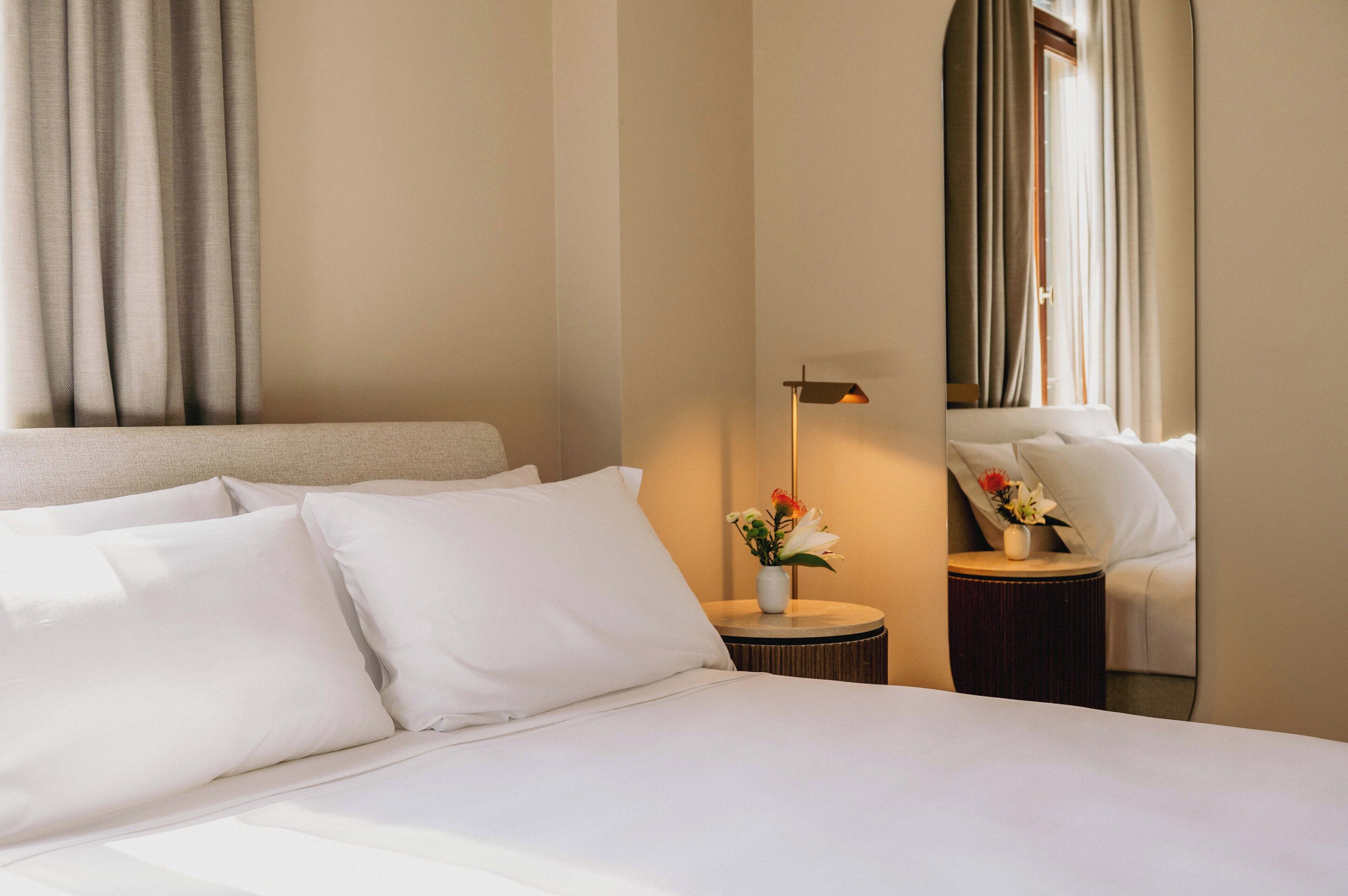 Una habitación de hotel con cama, una mesita de noche con lámpara y una ventana con cortinas.
