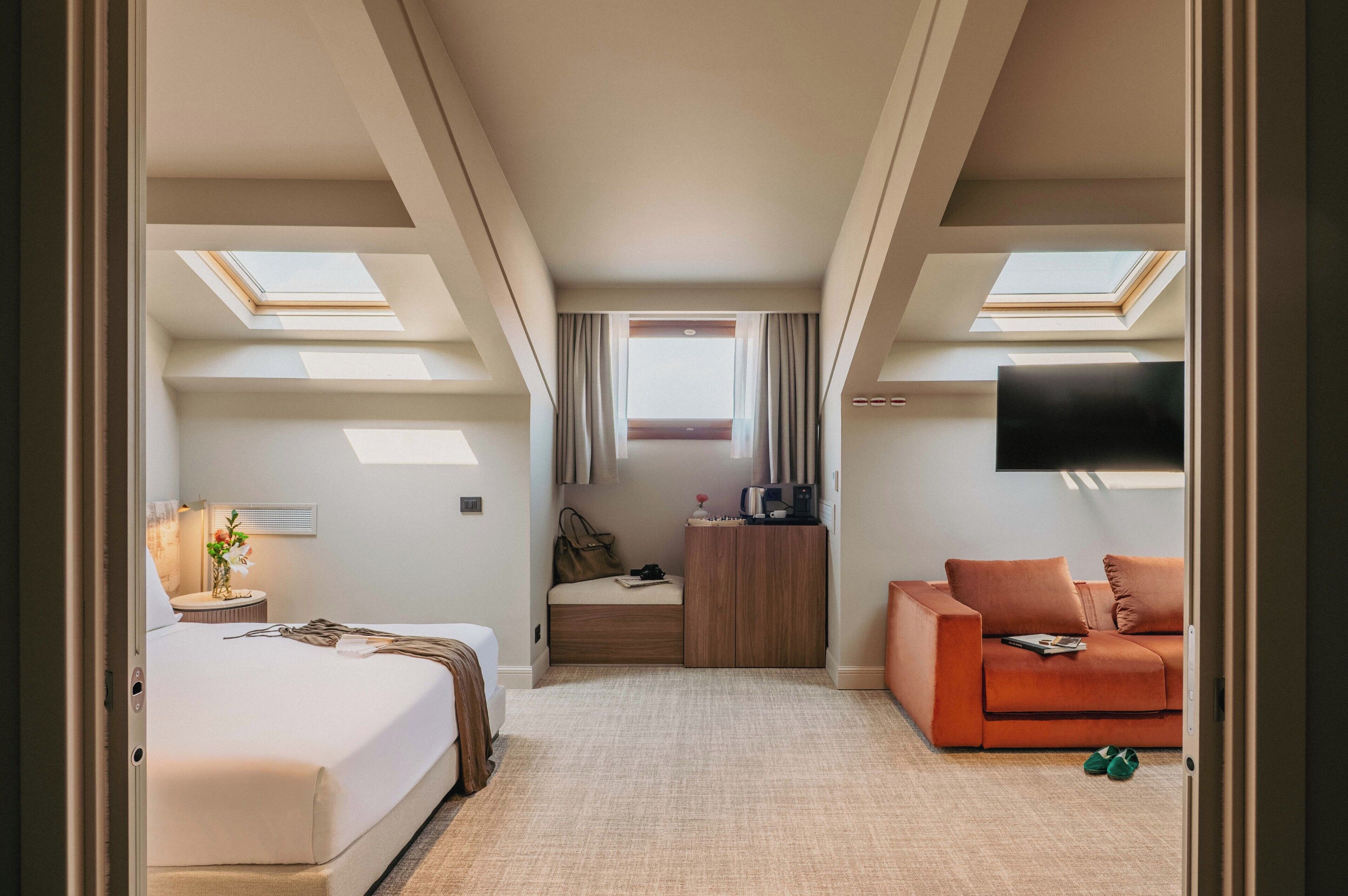 A hotel room with a bed, a sofa, a TV, a desk, and a window with curtains.