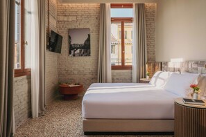 Een hotelkamer met een bed, een klein nachtkastje, een schilderij aan de muur en uitzicht op gebouwen.