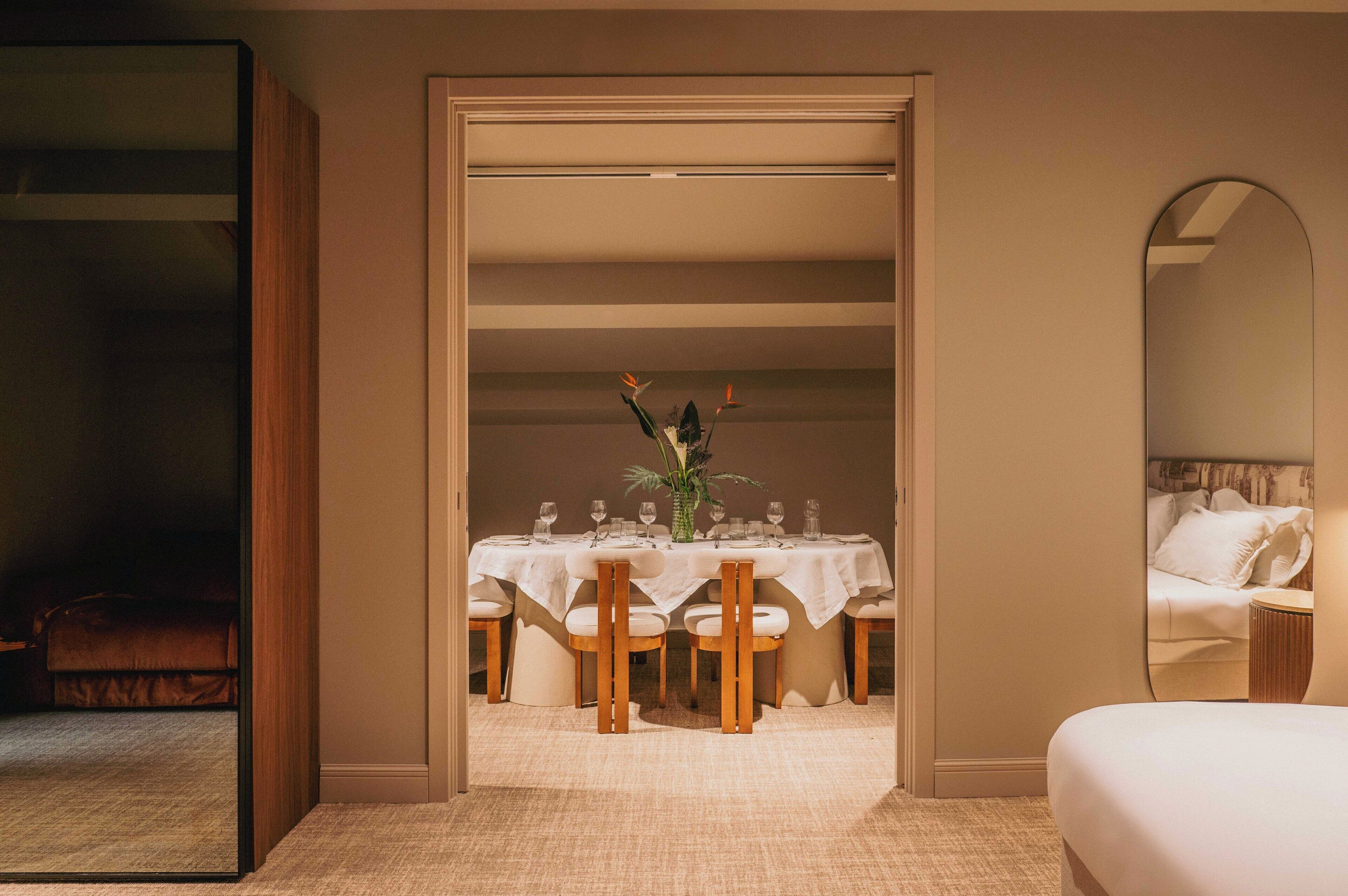 A hotel room with a dining area, a bed, and a mirror.