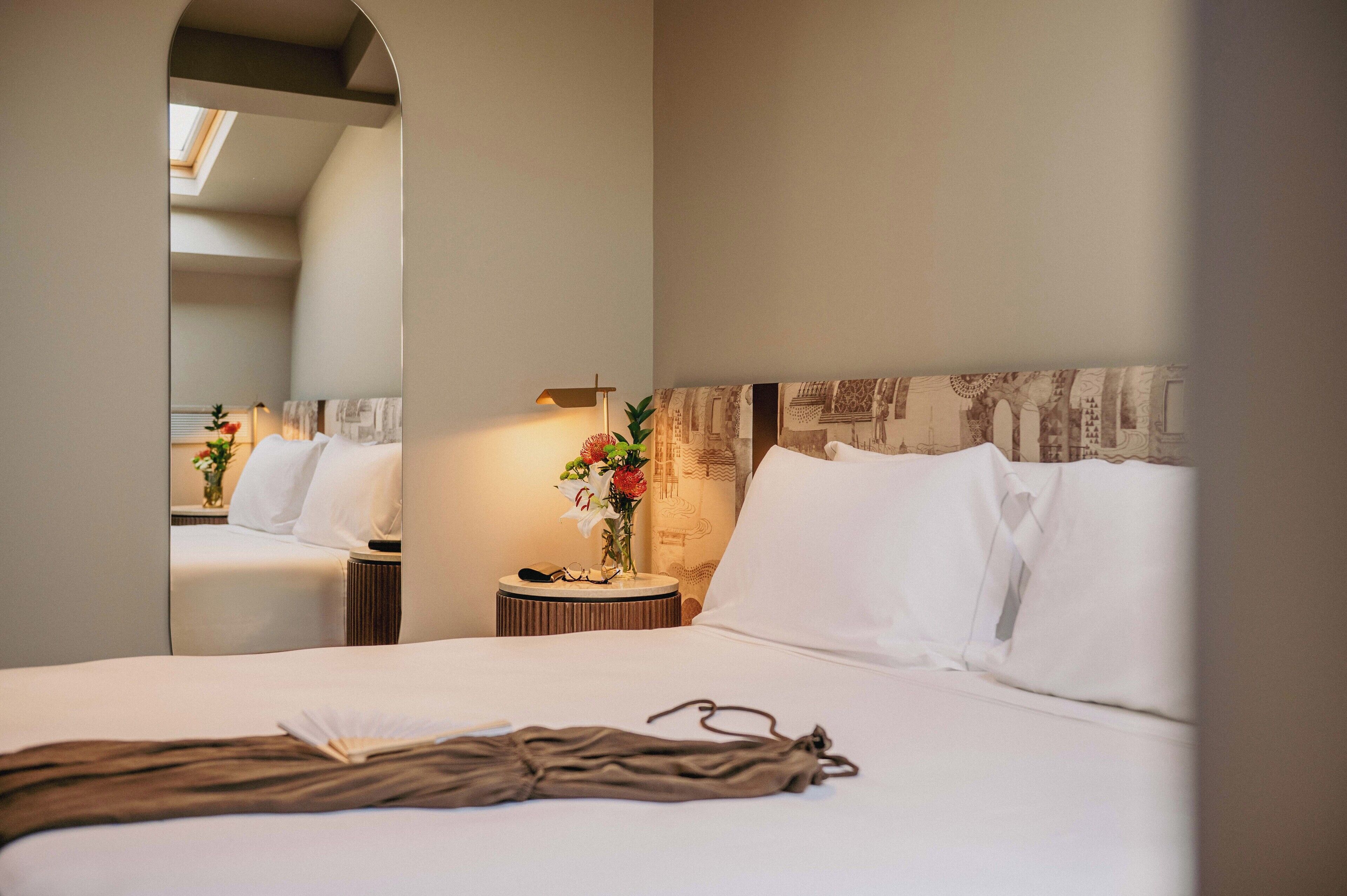 Ein Hotelzimmer mit einem großen Bett, einem Nachttisch mit Lampe, einem Spiegel und einem dekorativen Kopfteil.