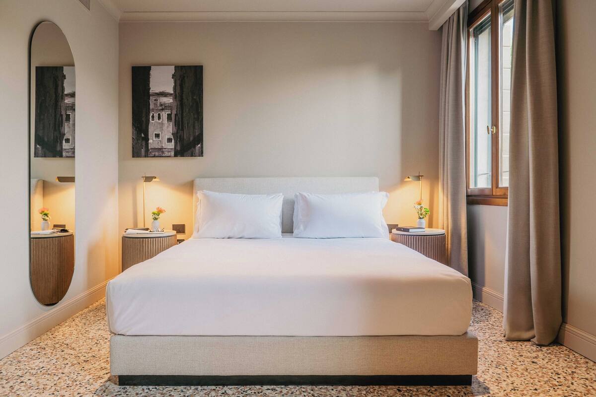 A hotel room with a large bed, two bedside tables with lamps, a mirror, and a framed picture on the wall.