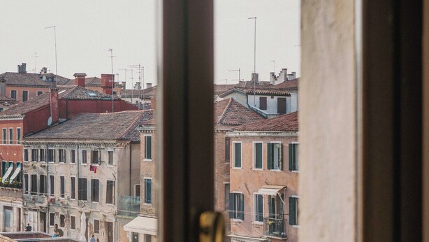 A view through a window of a Venetian canal with buildings and a bridge. - Rimon Place-Kosher (Venice)
