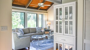 A modern living room with a sofa, two glass coffee tables, and a cabinet with glass doors. - Sunset Rentals | Night Heron 55 (Hilton Head Island)