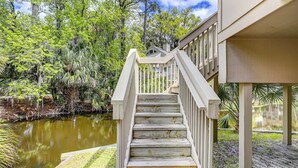 A wooden staircase leading to a building with a view of a pond and surrounding trees. - Sunset Rentals | Night Heron 55 (Hilton Head Island)