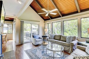 A spacious living room with a high ceiling, large windows, and a ceiling fan. - Sunset Rentals | Night Heron 55 (Hilton Head Island)