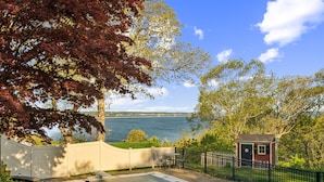 A patio with a view of the water, a small shed, and a white fence. - Coastal Comfort With Stunning Harbor Views 3 Bedroom Home (Plymouth)