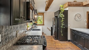 A kitchen with dark cabinetry, a gas stove, a sink, and a refrigerator. - Coastal Comfort With Stunning Harbor Views 3 Bedroom Home (Plymouth)