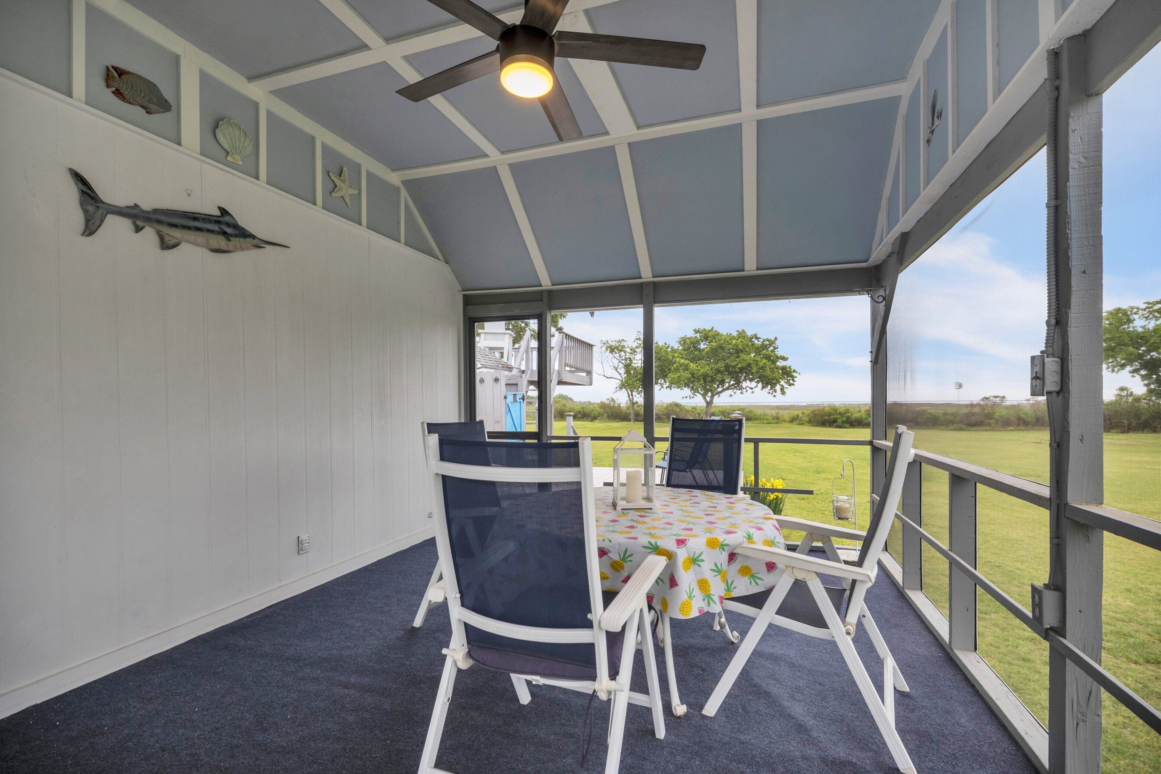 A covered outdoor area with a ceiling fan, a table with chairs, and a view of the outdoors.