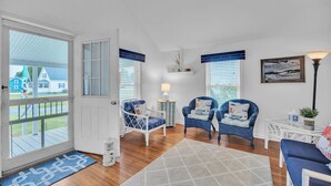 A spacious living room with a large sliding glass door leading to a deck, two blue patterned chairs, a white sofa, and a small table with a lamp. - Oyster Cottage In Historic Fishing Village 2 Bedroom Cottage (Cape Charles)