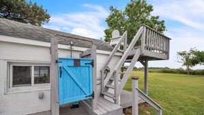 A wooden deck with a blue gate, a staircase, and a view of a grassy field. - Oyster Cottage In Historic Fishing Village 2 Bedroom Cottage (Cape Charles)