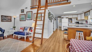 A spacious living area with a loft bedroom, wooden flooring, white furniture, and a kitchen with a bar area. - Oyster Cottage In Historic Fishing Village 2 Bedroom Cottage (Cape Charles)