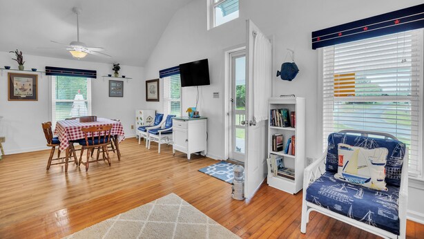 A spacious room with a dining table, chairs, a ceiling fan, a TV, and a bookshelf. - Oyster Cottage In Historic Fishing Village 2 Bedroom Cottage (Cape Charles)