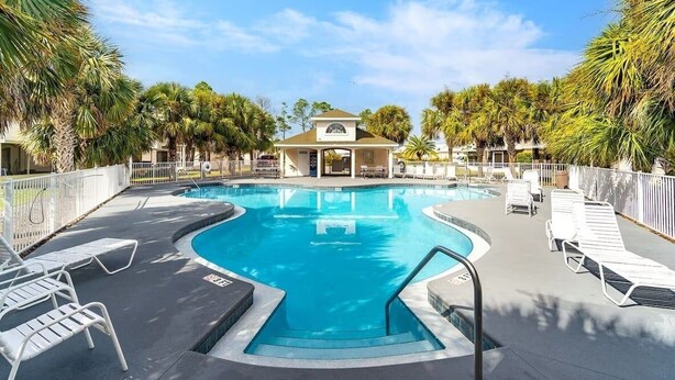 A swimming pool with lounge chairs and a covered area, surrounded by palm trees. - 225 Seahorse Way 3 Bedroom Home (Panama City Beach)