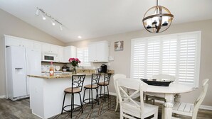 A kitchen with white cabinets, a central island with bar stools, a dining table with chairs, and a chandelier. - 225 Seahorse Way 3 Bedroom Home (Panama City Beach)