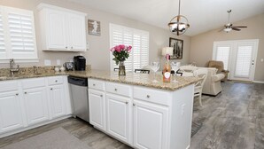 A kitchen with white cabinets, a granite countertop, and a dining area with a table and chairs. - 225 Seahorse Way 3 Bedroom Home (Panama City Beach)