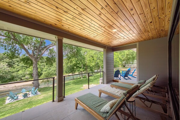A covered outdoor area with wooden ceiling, green lounge chairs, and a view of a grassy landscape. - Cl 970 Water You Waiting For? 4 Bedroom Home (Canyon Lake)