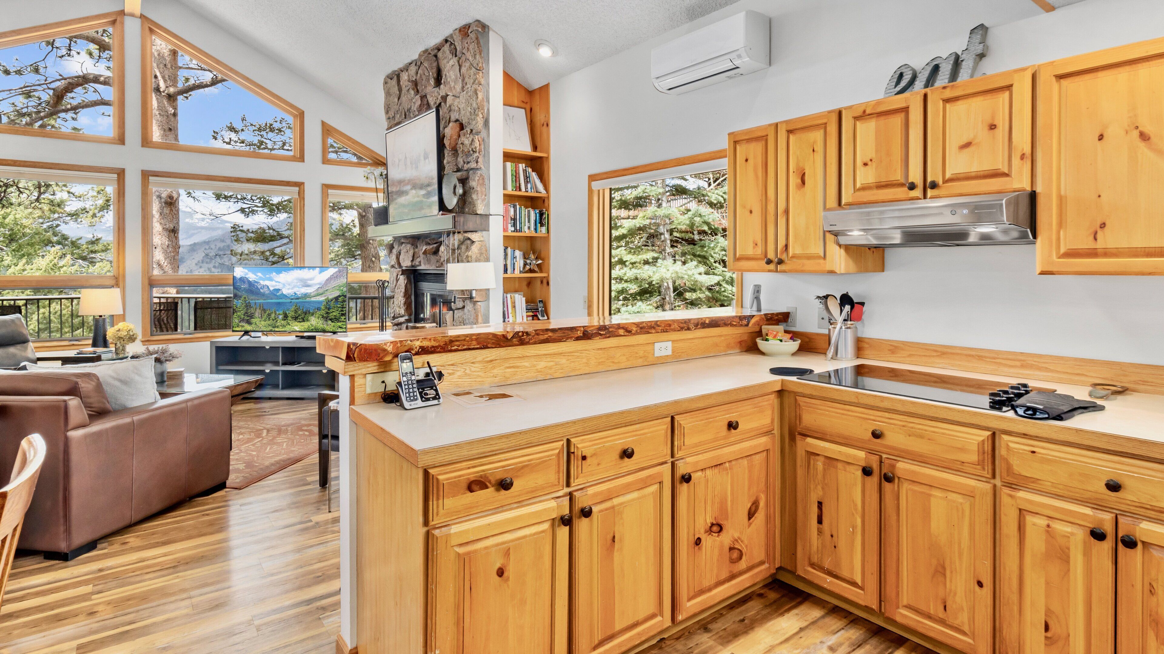 A modern kitchen with wooden cabinets, a stone accent wall, and a large window overlooking a forest.