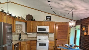 Una cocina con armarios de madera, un refrigerador de acero inoxidable, un microondas, un horno y una mesa de comedor con sillas.