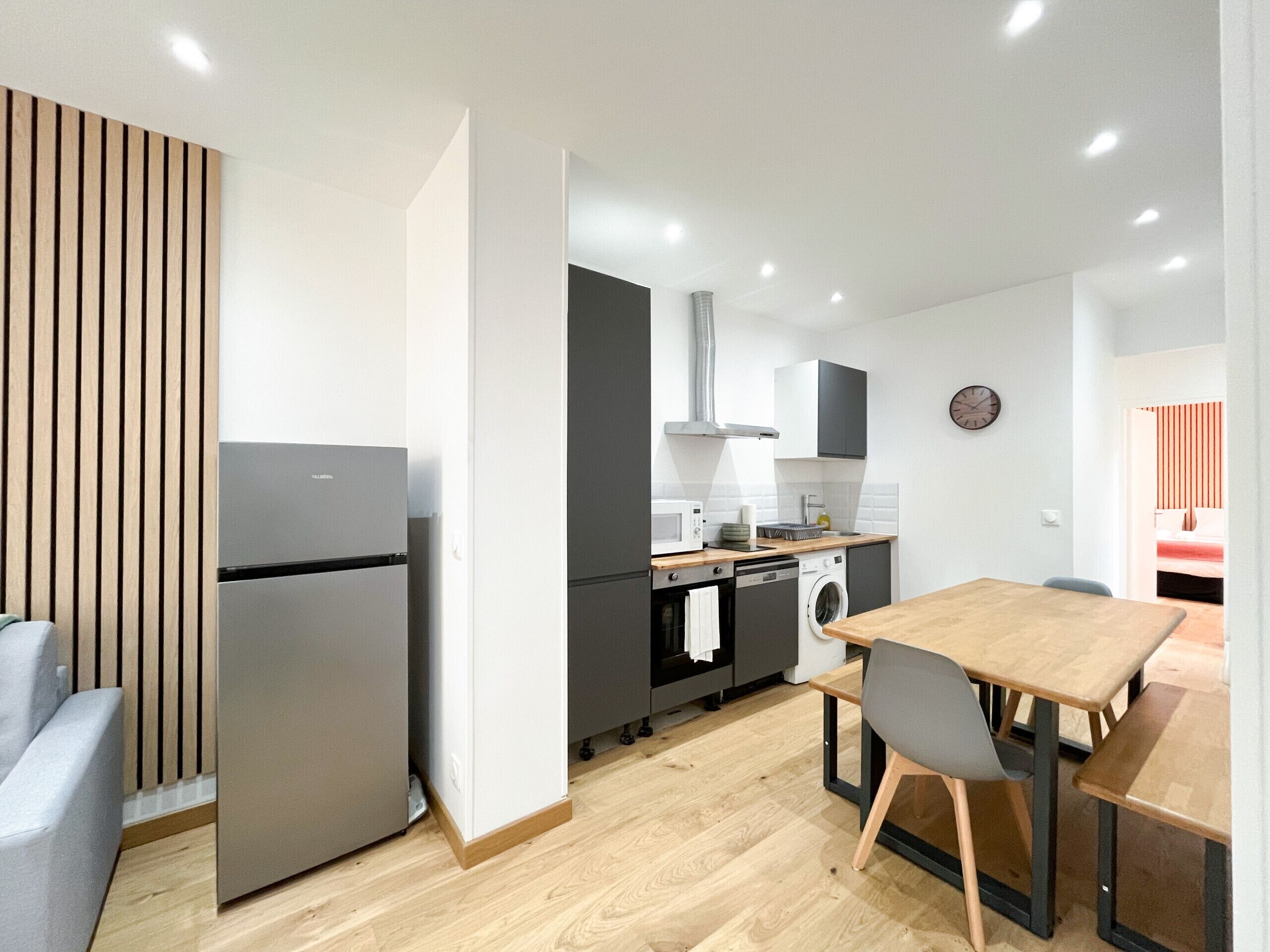 Una cocina moderna equipada con horno, microondas y lavadora. Hay una zona de comedor con una mesa y sillas de madera.