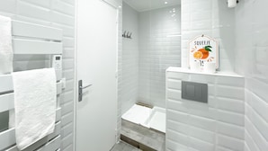 A modern bathroom with white tiles, a glass shower enclosure, a towel rack, and a sign that reads "SQUEEZE THE ORANGE."