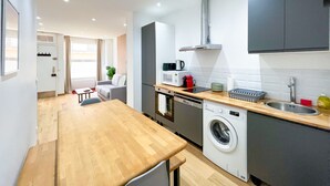 A modern kitchen with a wooden table, a washing machine, a microwave, and a sink.