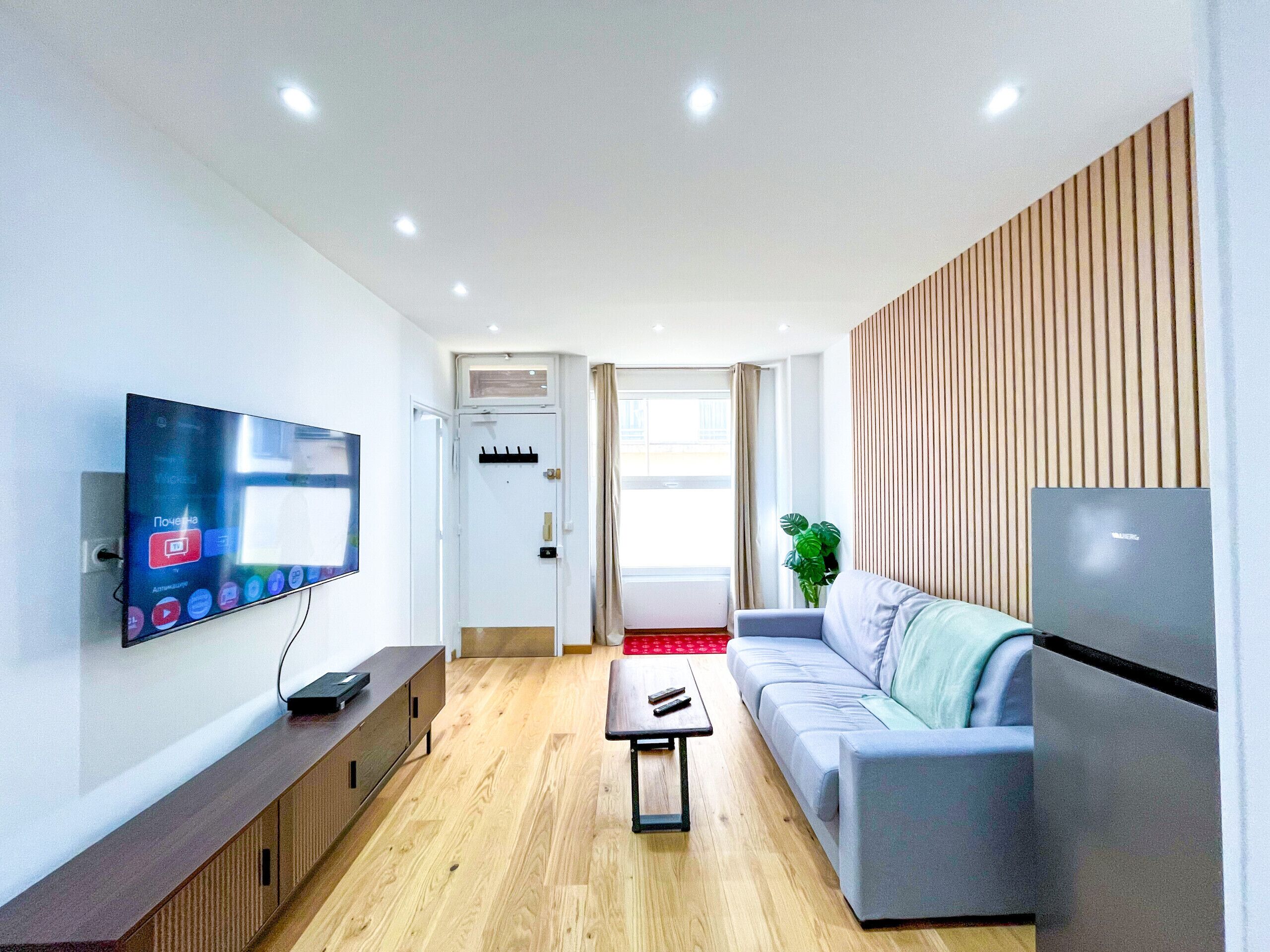 A modern living room with a flat-screen TV mounted on the wall, a grey sofa, a wooden coffee table, and a built-in entertainment unit.