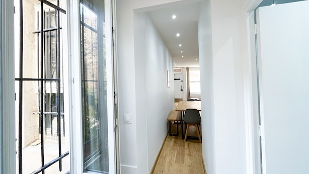 A narrow hallway with a wooden floor leading to a dining area with a table and chairs.