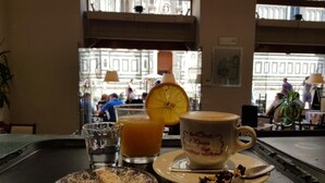 A table with a coffee cup, a glass of orange juice, and a slice of cake. - LunArt (Florence)