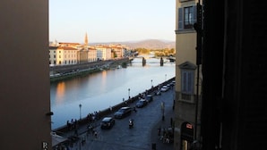 A riverside view with buildings, a bridge, and parked cars. - LunArt (Florence)
