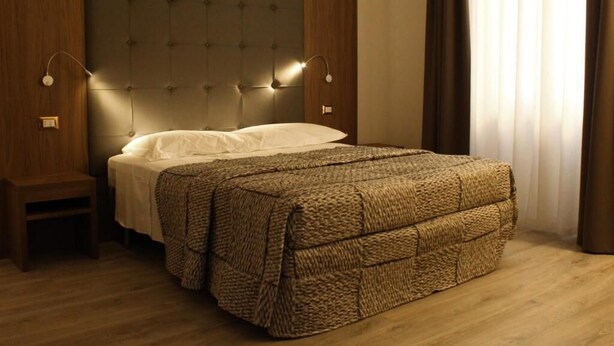 A bedroom with a tufted headboard, a bed with a textured blanket, a nightstand, and two wall-mounted lamps. - LunArt (Florence)
